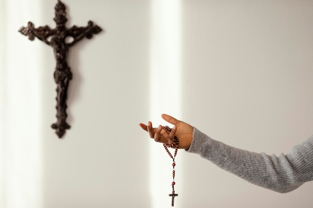 Religious woman praying with rosary beads at home