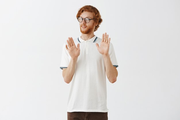 Reluctant bearded redhead guy posing against the white wall with glasses