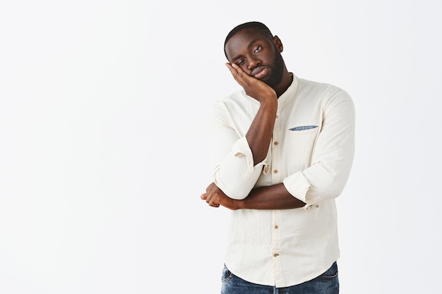 Reluctant and bored young guy posing against the white wall