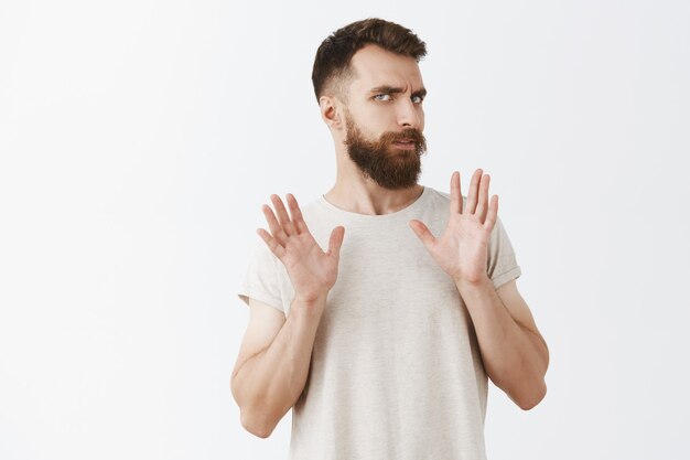 Reluctant and bothered bearded man posing against the white wall