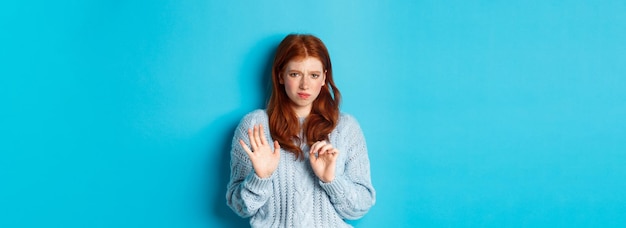 Foto gratuita ragazza rossa riluttante che chiede di stare alla larga stringendo la mano nel gesto di rifiuto rifiuta l'offerta e la grima