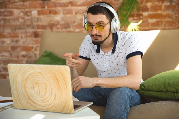 Remote meeting. Man working from home during coronavirus or COVID-19 quarantine, remote office concept. Young businessman, manager doing tasks with smartphone, computer, has online conference.