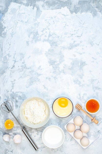 Удаленный вид на белую муку в миске и нержавеющий инструмент для приготовления пищи, яйца, ломтик лимона на двухцветном фоне
