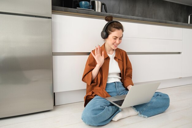 Free photo remote workplace young woman works from home sits on floor with headphones and laptop student doing