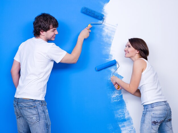 Renovation by laughing cheerful loving couple brushing the wall