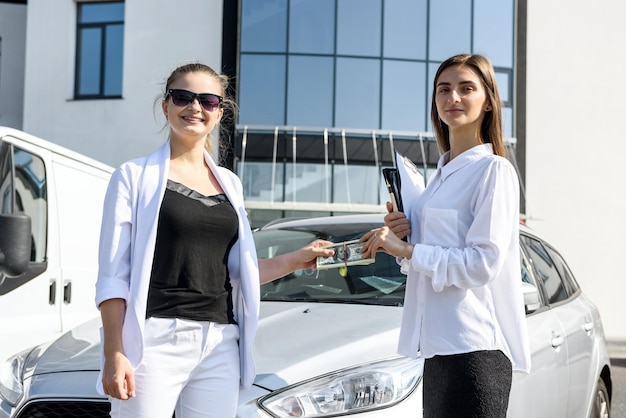 Rent or car buy concept. two women with dollar bundle posing near car