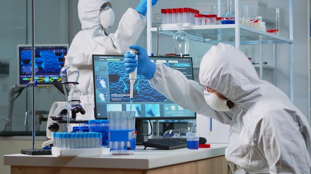 実験室でマイクロピペット充填試験管を使用して保護スーツを着た科学者を研究します。 covid19に対する治療法の開発を分析するハイテクを使用してウイルスの進化を調べる微生物学者のチーム。