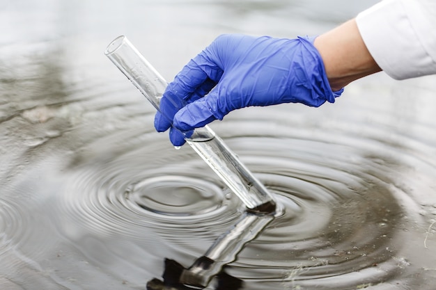 Foto gratuita il ricercatore tiene una provetta con acqua in una mano in un guanto blu