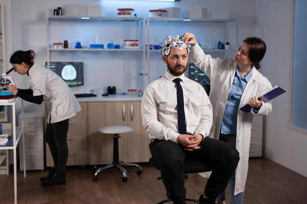 Researcher neurologist woman adjusting eeg headset monitoring brain activity of man patient during medical experiment in modern laboratory. Scientist doctor analyzing nervous system. Medicine service