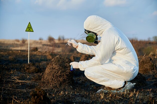 Researcher in protective suit working on a burnt field taking samples of flora