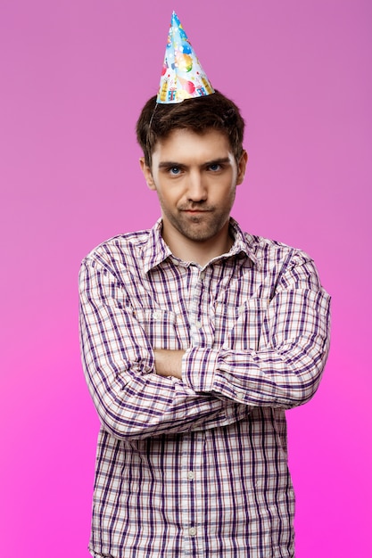 Resentful handsome man posing over purple wall. Birthday party.