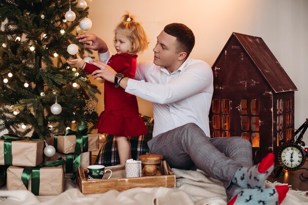 Responsible man assisting cute child with putting decorations on Christmas tree