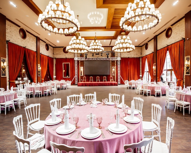 Restaurant hall with small stage monitor, red curtains, brick walls white napoleon chairs