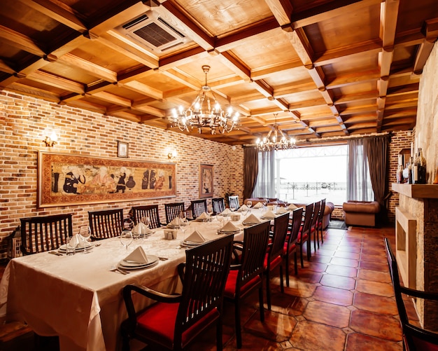 Restaurant table for 14 persons at restaurant hall with brick walls, wide windows and wood ceiling