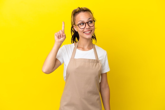 Русская девушка официант ресторана изолирована на желтом фоне, намереваясь реализовать решение, подняв палец вверх