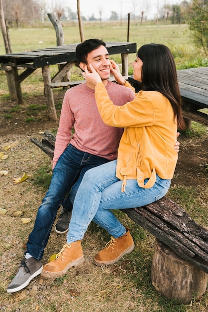 Resting happy pair having fun at wooden bench in autumn park