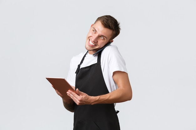 Retail stores, small business, cafe and restaurants takeaway concept. Handsome young shop manager, employee receiving order over phone, talking with customer and writing down info in digital tablet