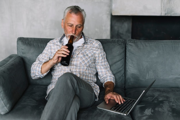 노트북을 사용 하여 병에서 맥주를 마시는 은퇴 한 남자