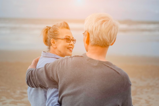 海沿い​に​座っている​引退​カップル​、​女性​は​夫​を​抱きしめ​、​朝​の​ビーチ​で​お互い​を​見つめ​、​引退​コンセプト​の​生命​保険​プラン​。