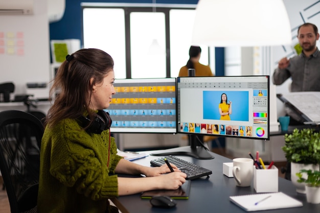 Редактор ретушера женщина работает на компьютере с двумя мониторами и стилусом