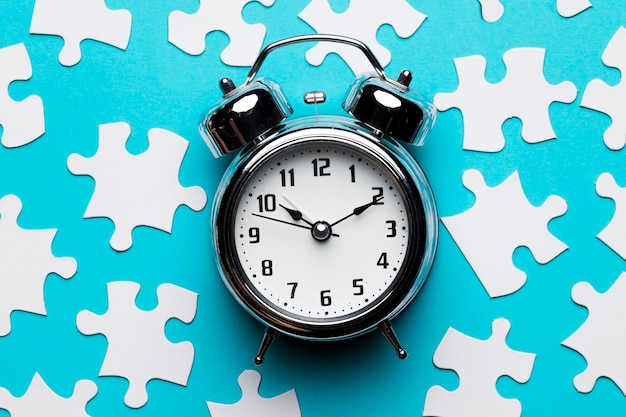 Retro alarm clock and jigsaw puzzle pieces on blue backdrop