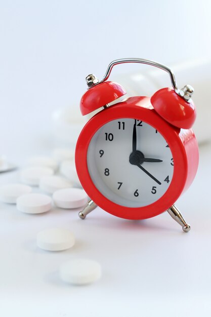 レトロな目覚まし時計と白い錠剤のクローズアップ。健康管理