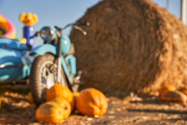 Foto gratuita motocicletta blu retrò con zucche e balle di fieno accanto a un soleggiato giorno d'autunno vista frontale sfocata