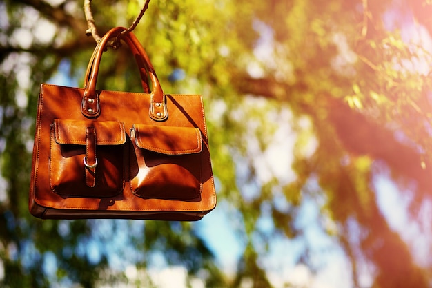 Retro brown  man leather bag  in bright colorful summer park hanging on leafes