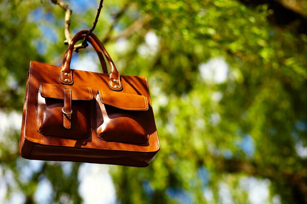 retro brown  man leather bag  in bright colorful summer park hanging on leafes