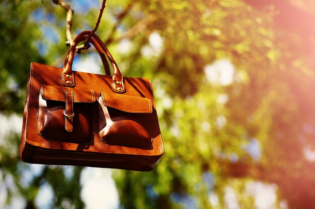 Ретро коричневая мужская кожаная сумка в ярком красочном летнем парке висит на листве
