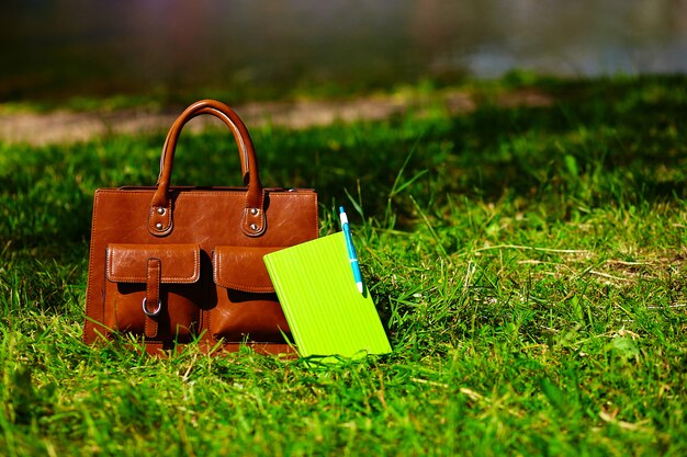 Retro brown  man leather bag and notebook in bright colorful summer grass in the park