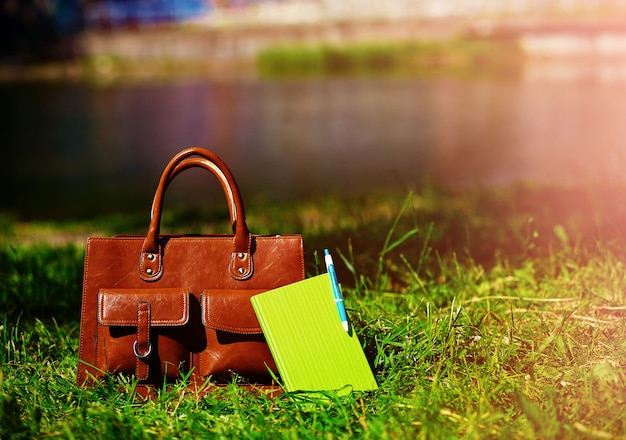 Retro brown  man leather bag and notebook in bright colorful summer grass in the park