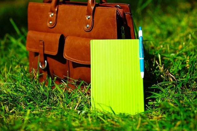 Retro brown  man leather bag and notebook in bright colorful summer grass in the park