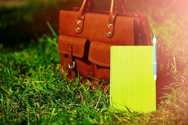 Retro brown  man leather bag and notebook in bright colorful summer grass in the park