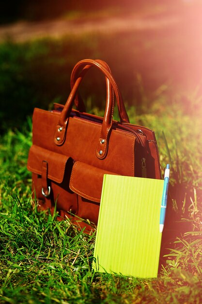 Retro brown  man leather bag and notebook in bright colorful summer grass in the park