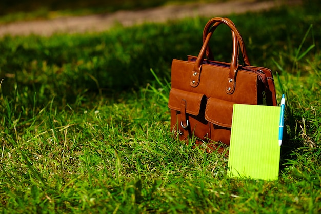 공원에서 밝고 화려한 여름 잔디에서 레트로 갈색 남자 가죽 가방 및 노트북
