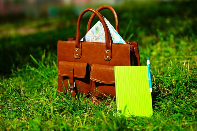 レトロな茶色の男革バッグと公園の明るいカラフルな夏の草のノート