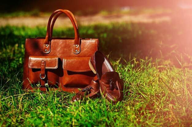 Retro brown shoes and man leather bag in bright colorful summer grass in the park