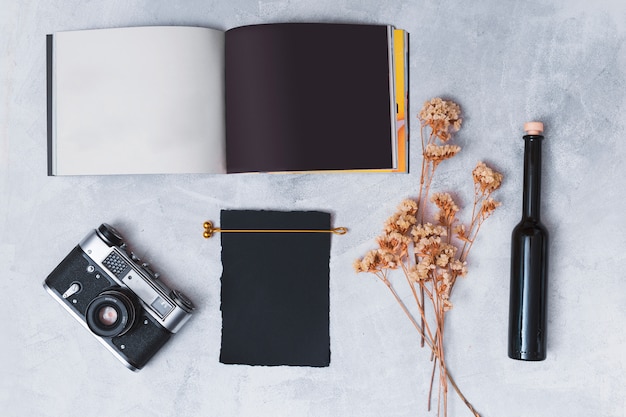 Retro camera near dark paper, dry plant twigs, notebook and bottle