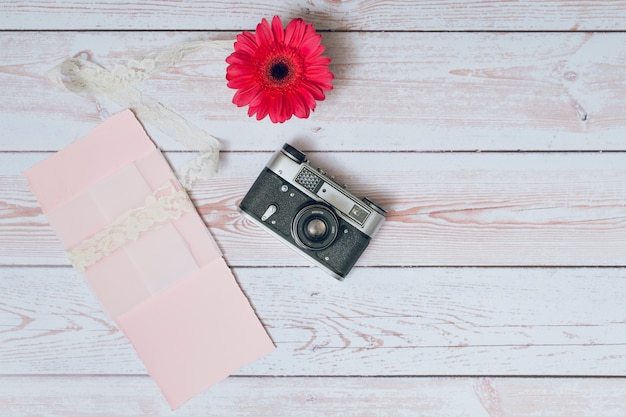 Retro camera near set of papers and fresh flowers