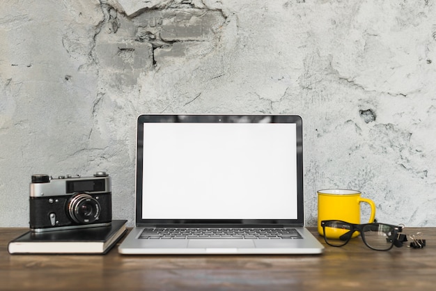 Retro camera and open laptop with office stationeries on wooden table