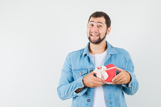 Retro-style man in jacket,t-shirt holding mini gift box and looking merry , front view. space for text