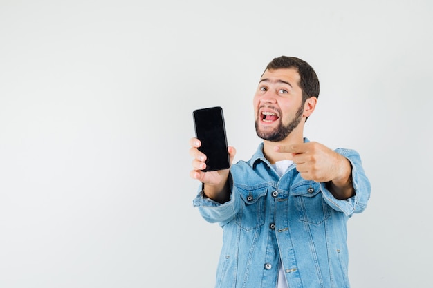 Retro-style man in jacket,t-shirt pointing at mobile phone and looking positive , front view.