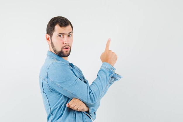 Retro-style man in jacket,t-shirt pointing up and looking focused , front view.