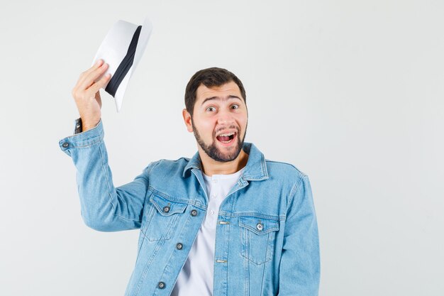 Retro-style man in jacket,t-shirt taking off his hat and looking glad , front view.