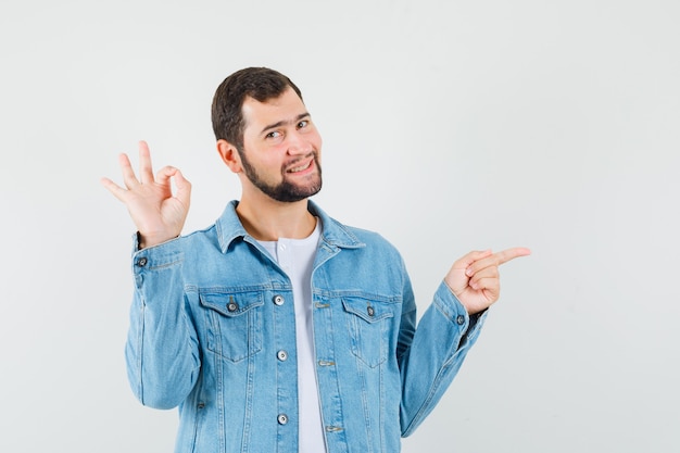 Retro-style man showing ok gesture while pointing away in jacket,t-shirt and looking glad , front view.