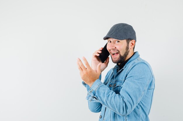 Retro-style man talking on phone in jacket,cap,shirt and looking amused , front view. space for text