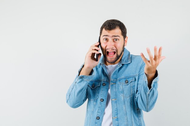 Retro-style man talking on phone in jacket,t-shirt and looking optimistic. front view. space for text