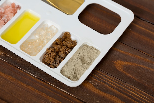 Rhassoul clay; coffee grounds; rock salt and oil on white tray against wooden table