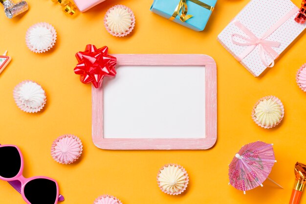 Ribbon bow on wooden white frame surrounded with sunglasses; gift boxes and aalaw on yellow backdrop